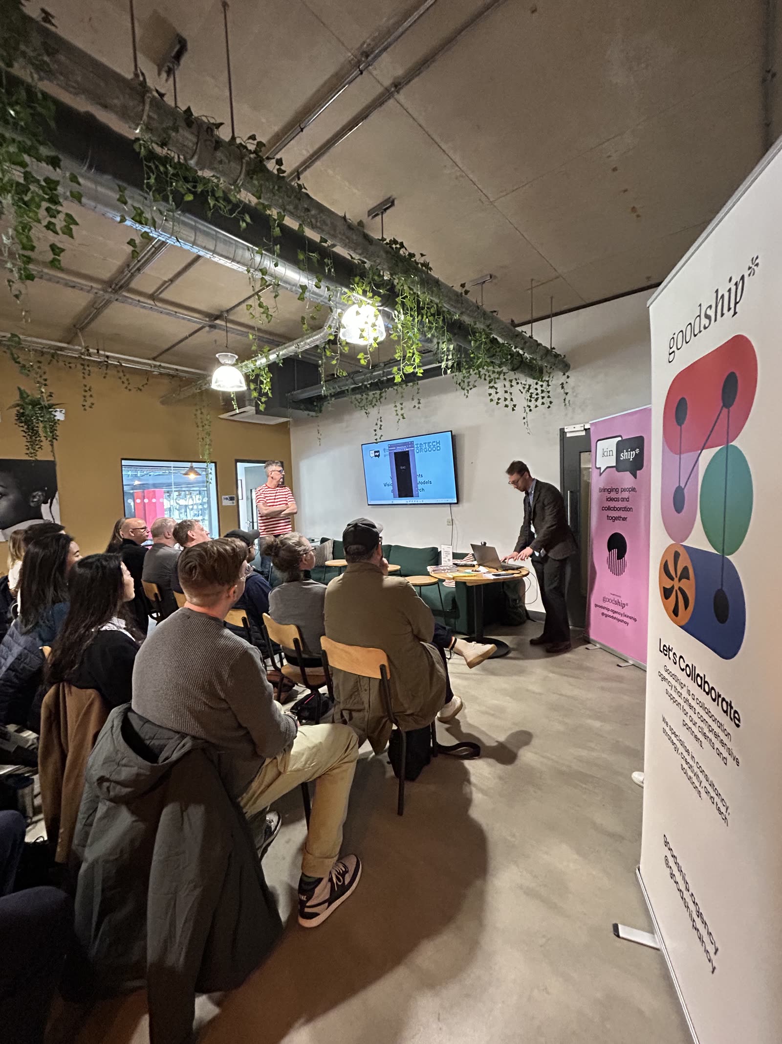 An audience seated in a Liverpool workspace watching an AI & Tech for Good talk, with GoodShip* and KinShip* banners alongside the screen.