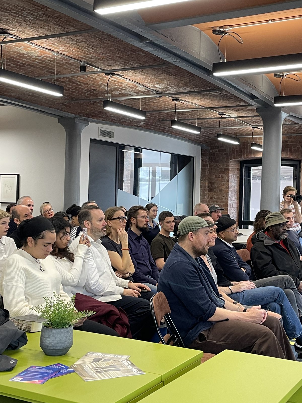 A diverse audience of technologists, businesses, educators and community leaders seated at a KinShip AI & Tech for Good session in a brick-walled Liverpool workspace